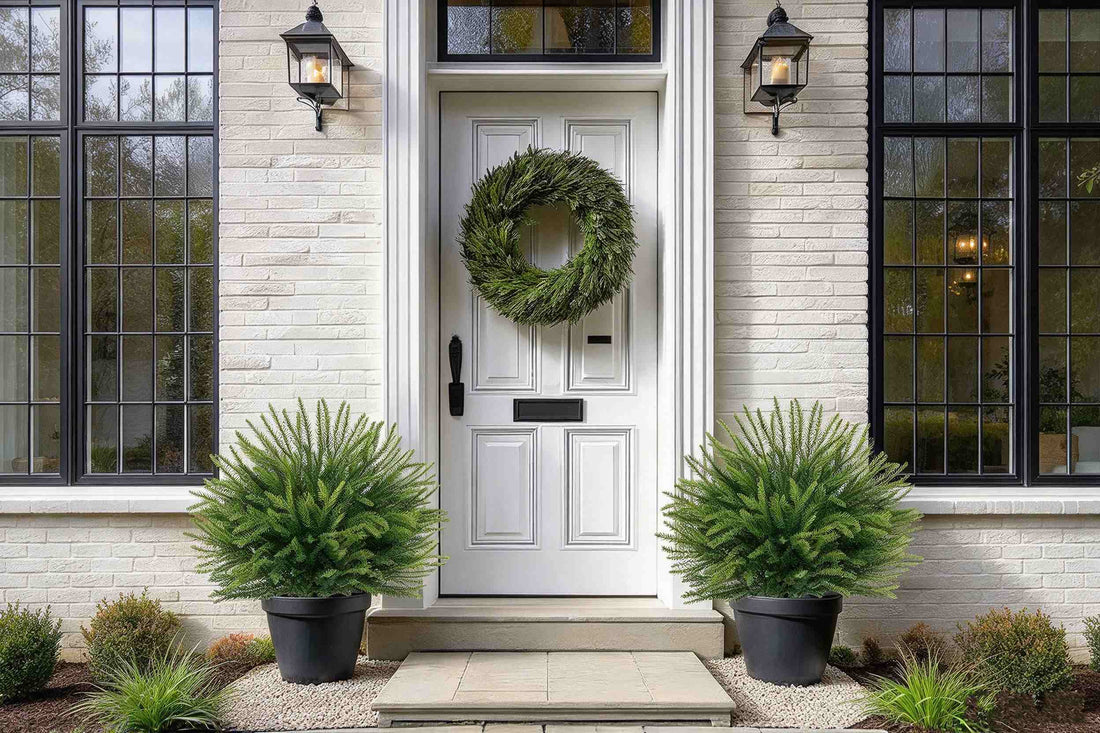 Two artificial christmas topiary green pine in black planters by white door with wreath for classic outdoor holiday decor