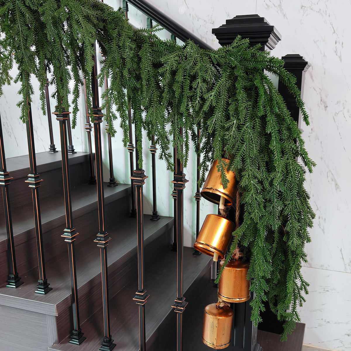 Lush drooping norfolk pine faux xmas garland decorated with vintage brass bells for staircase holiday decor