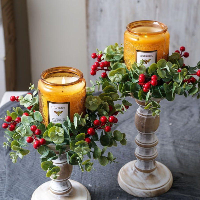 Two eucalyptus red berry candle rings with amber jar candles on vintage white candlesticks for holiday decor