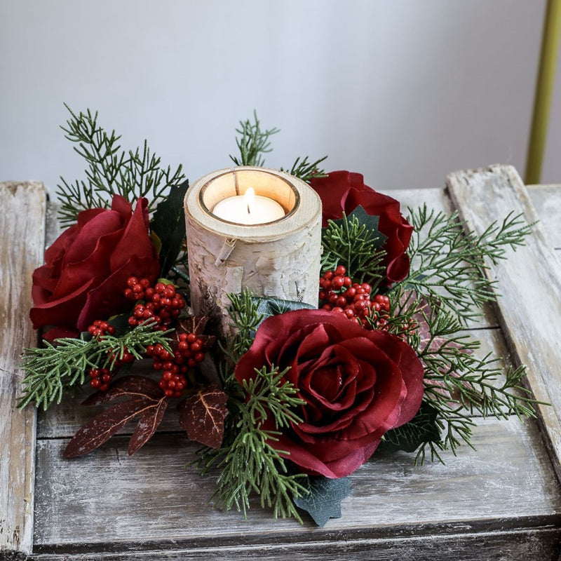 Christmas candle ring with burgundy artificial roses, red berries and cypress greenery paired with birch bark candle holder on rustic wooden table
