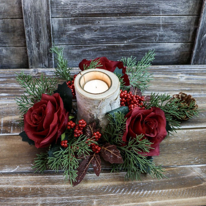 Artificial Christmas candle ring with deep red roses, bright red berries and cypress sprigs surrounding birch candle on weathered wood table