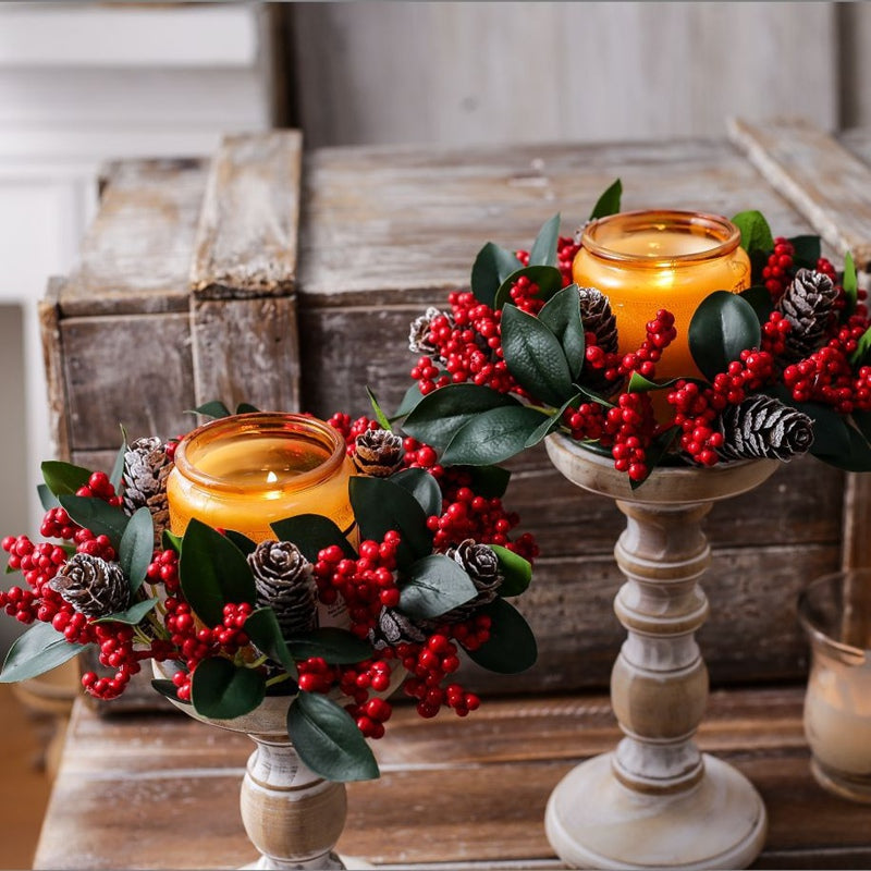 Christmas candle wreath holder with red berries pine leaves surrounding amber glass jar candle on rustic wooden table
