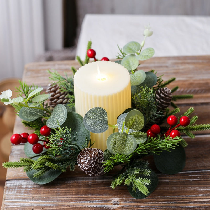 Christmas candle ring with eucalyptus, pine cones and red berries, paired with ribbed pillar candle on rustic wooden table