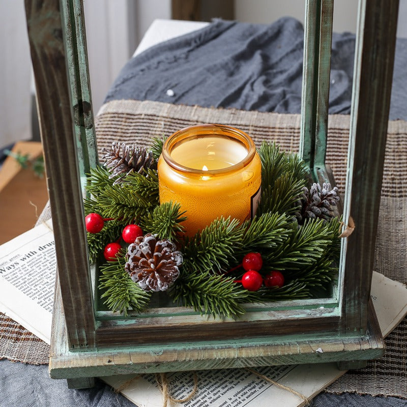 Christmas candle ring with pine, red berries and pinecones framing amber candle inside distressed green wooden lantern
