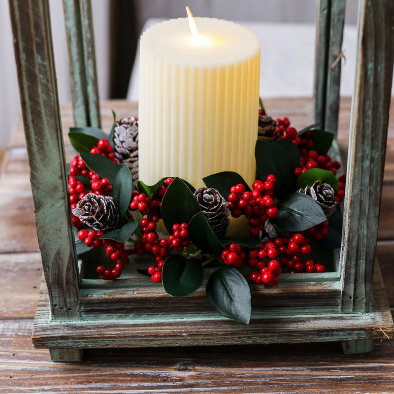 Small christmas candle ring wreath with red berries pine cones arranged around pillar candle inside vintage wooden lantern