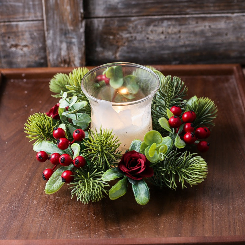 Christmas candle ring with red berries, burgundy roses, eucalyptus and pine greenery surrounding glass candle holder on rustic wooden tray
