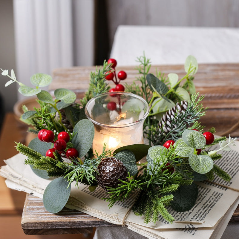 Close-up view of Christmas candle ring with eucalyptus leaves, red berries and frosted pine cone with lit pillar candle