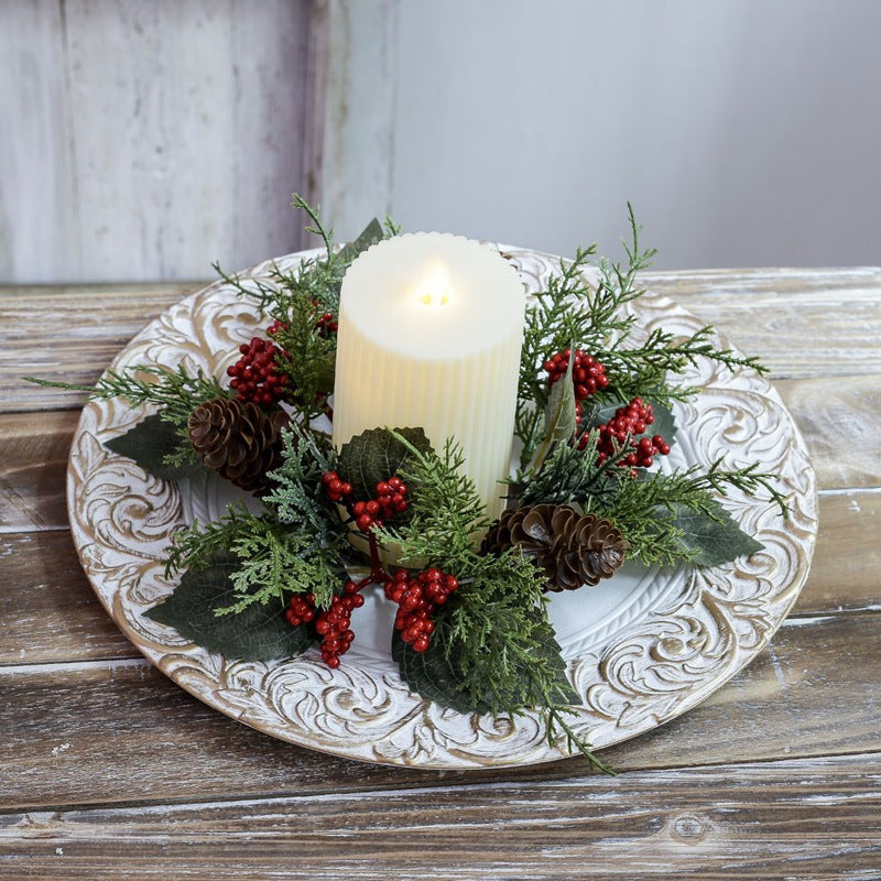 Pinecone and red berry candle ring surrounding fluted pillar candle, displayed on ornate white embossed plate for holiday table decor
