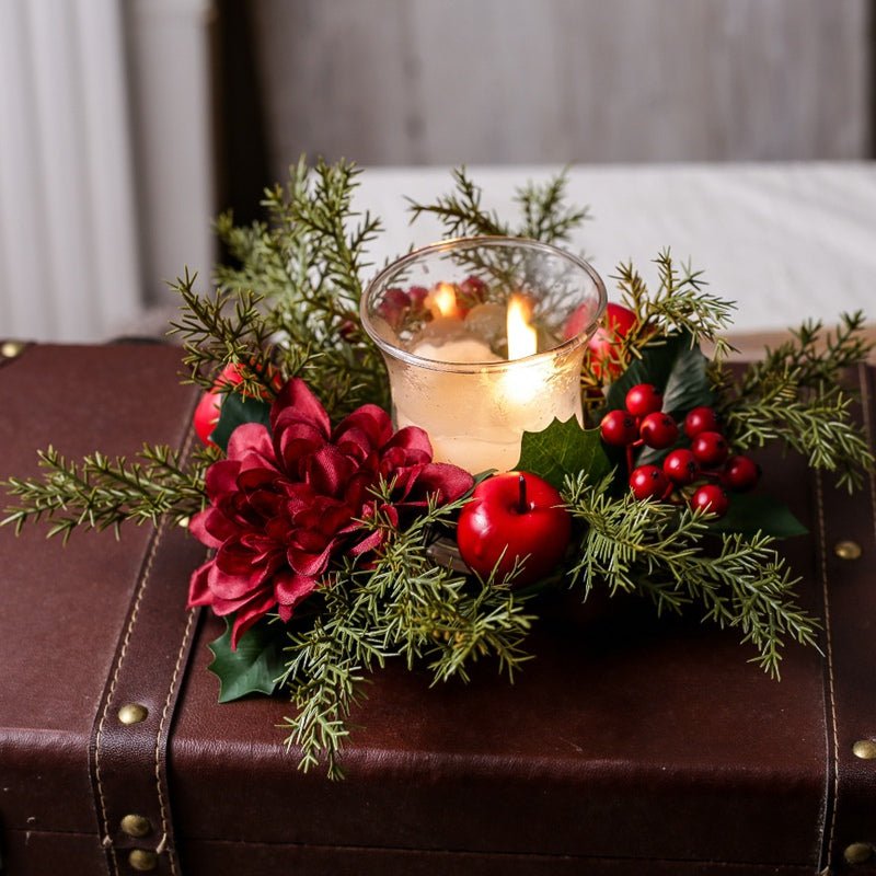 Christmas candle ring with burgundy dahlia, red berries and apples, lit glass candle arranged on vintage brown leather suitcase