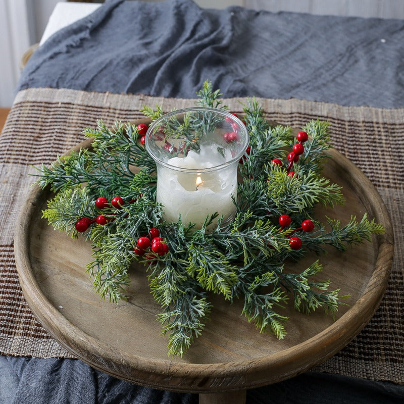 Green cypress red berry candle ring surrounding glass pillar candle on distressed white wooden candlestick for holiday table decor