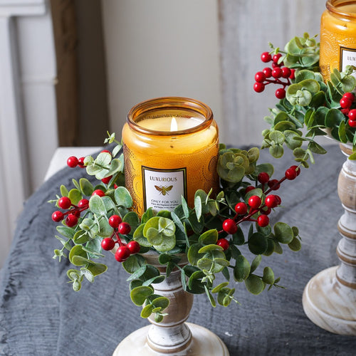 Two eucalyptus red berry candle rings with amber jar candles on vintage white candlesticks for holiday decor