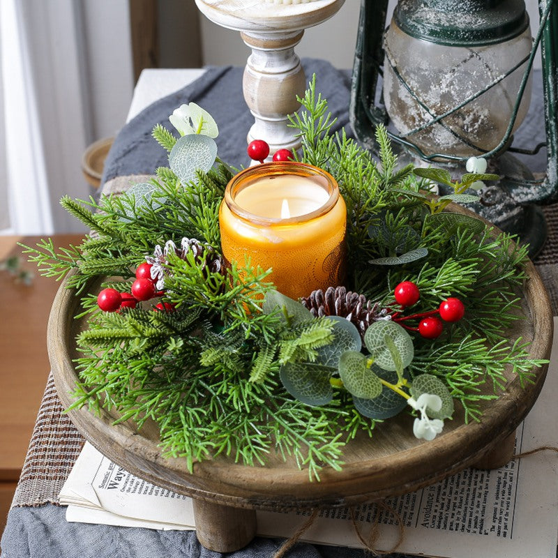 Winter candle ring decor with eucalyptus, pinecones and red berries around amber jar candle on vintage wooden tray