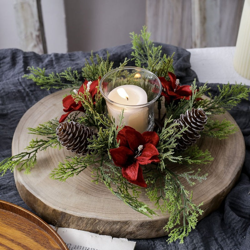 Holiday candle ring with red poinsettia blooms, frosted pinecones and cypress greenery placed on thick natural wood slice