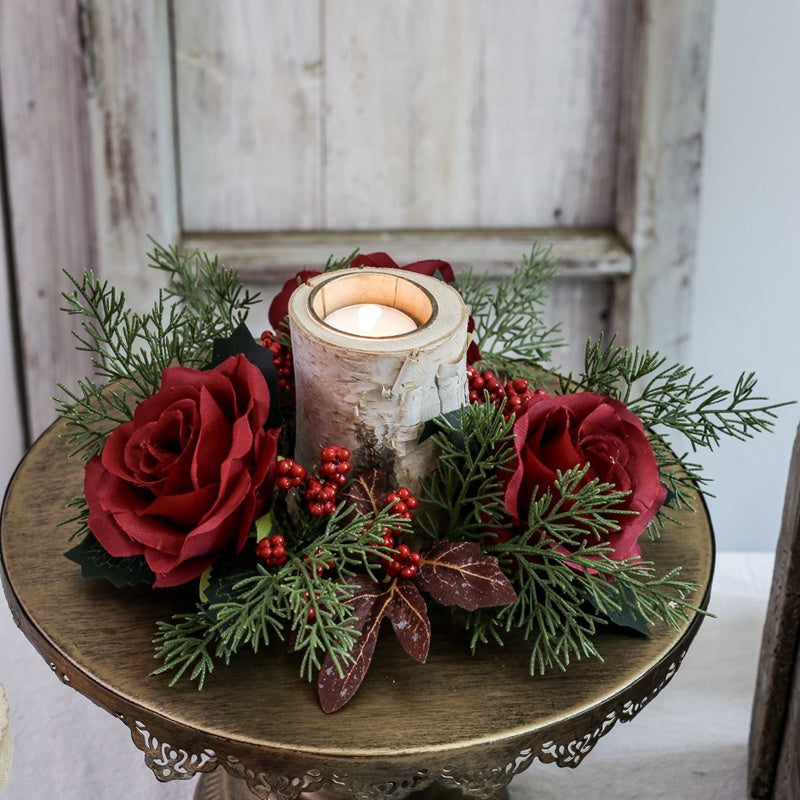 Festive burgundy rose candle ring with red berries and green cypress, arranged with birch candle on antique round metal display stand