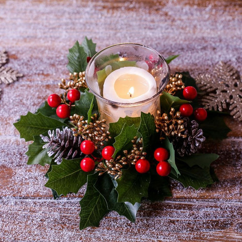 Close-up view of Christmas holly candle ring, red berries, frosted pinecone and green holly leaves around candle holder