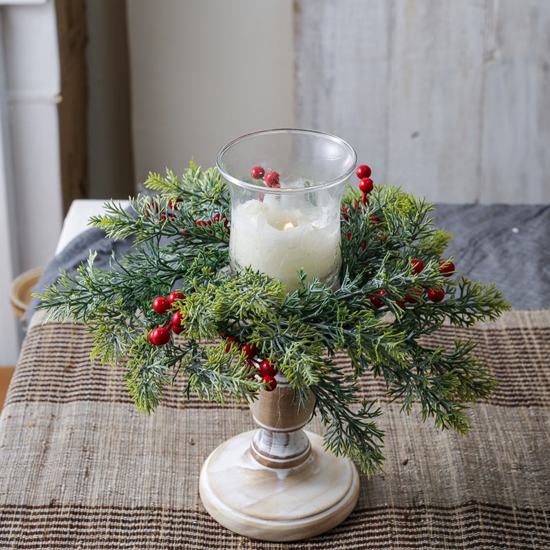 Green cypress red berry candle ring surrounding glass pillar candle on distressed white wooden candlestick for holiday table decor