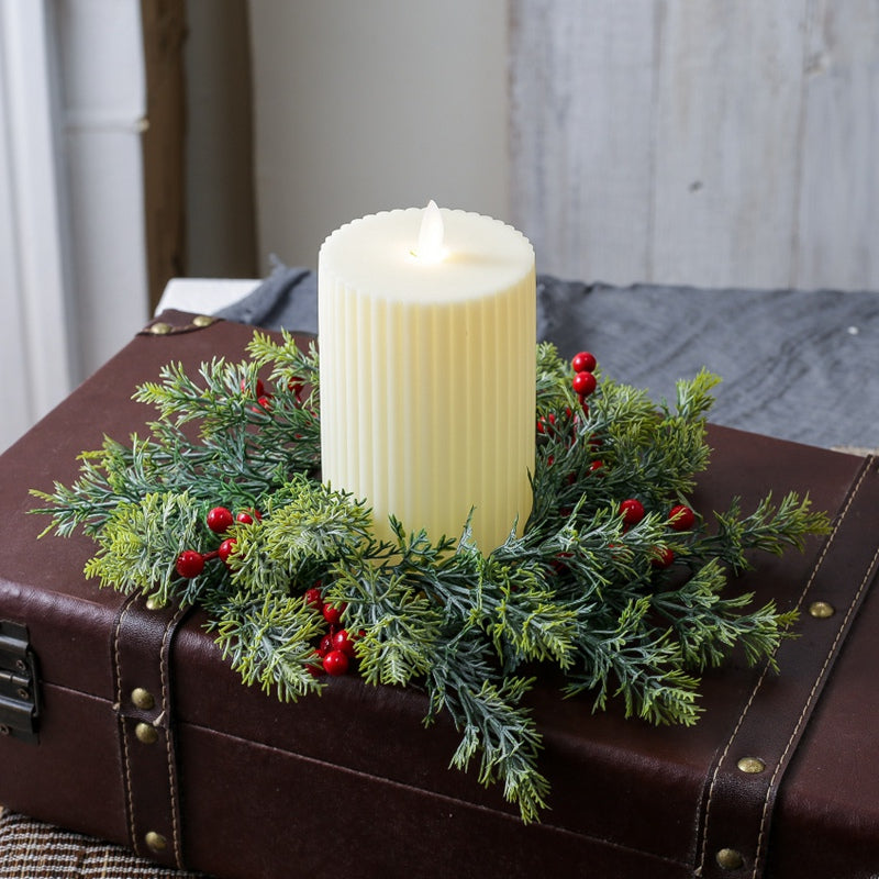 Christmas candle ring with artificial cypress foliage and bright red berries around ribbed pillar candle on vintage brown leather trunk