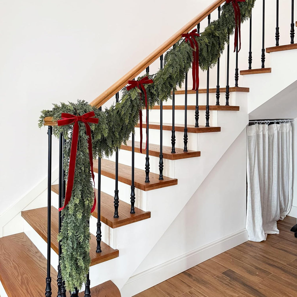 Lush drooping cedar christmas garlands decorated with red velvet bows for indoor wooden staircase holiday decor