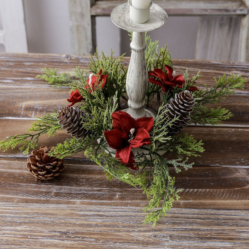 Empty Christmas candle ring decorated with red poinsettia flowers, pinecones and cypress greenery around distressed white wooden candlestick