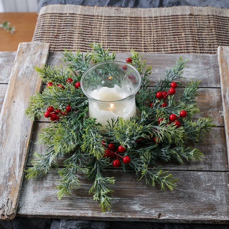 Artificial cypress and red berry candle ring with candle on weathered wooden plank, rustic Christmas table centerpiece decor