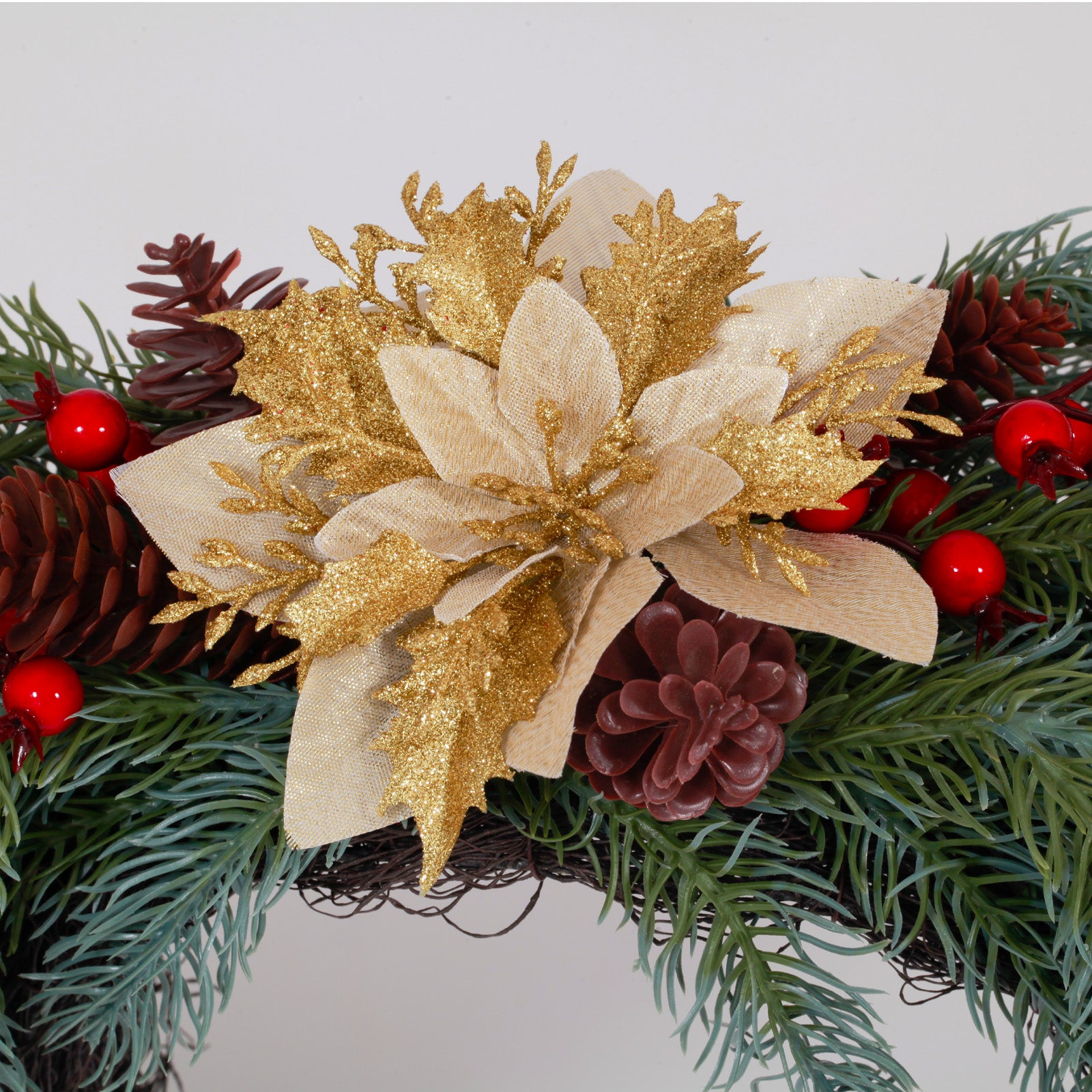 Closeup glitter gold poinsettia flower wreath accented with pinecones, red berries and reflective gold balls