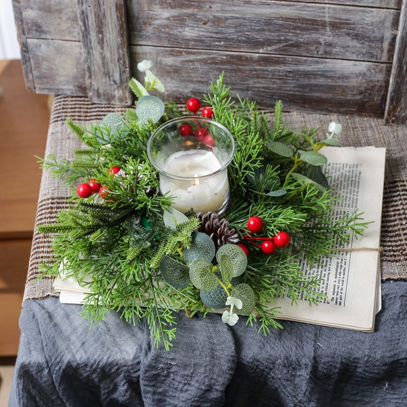 Christmas greenery candle ring with eucalyptus, pinecones and red berries surrounding glass candle on rustic table setting