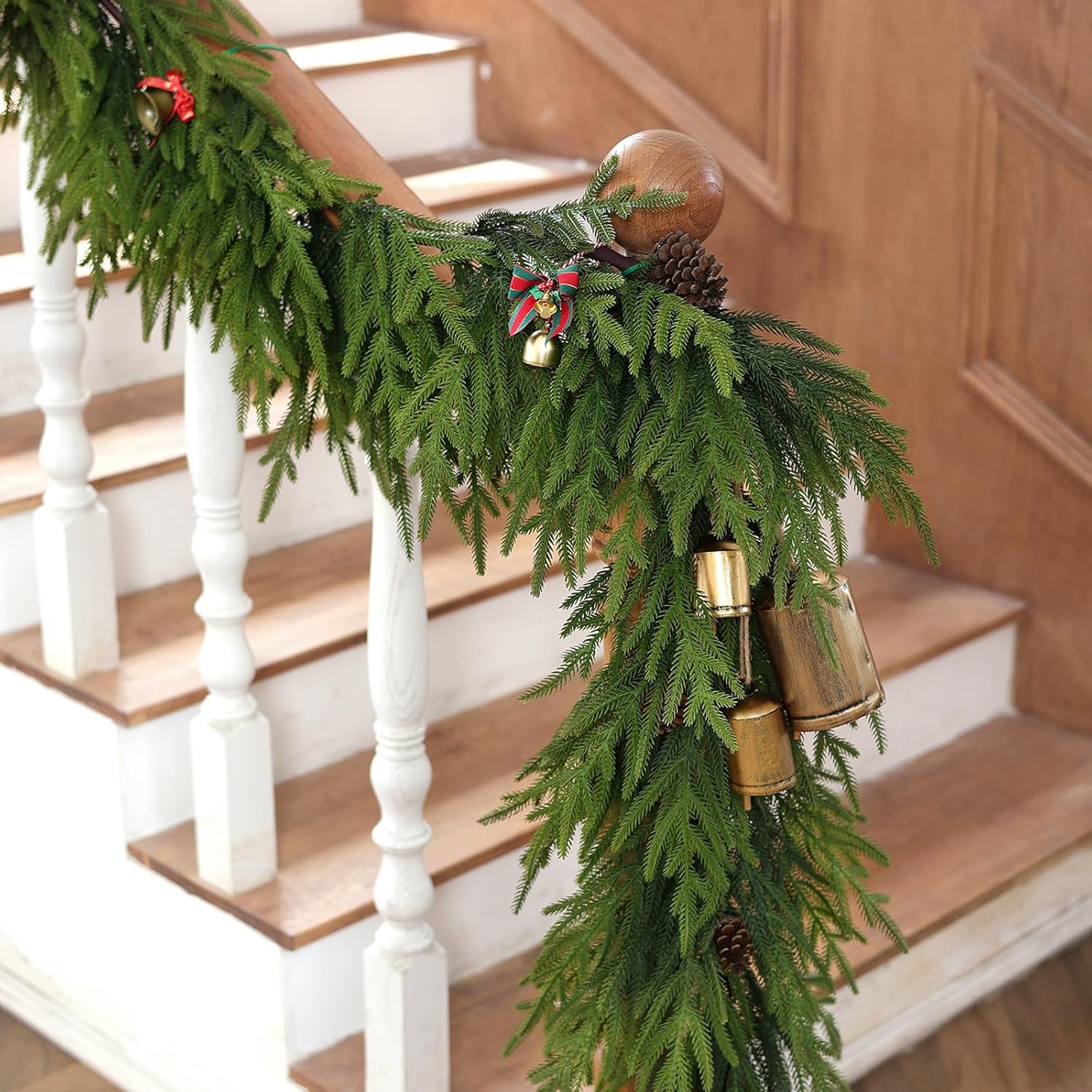 Long drooping Norfolk Pine Garland draped on white stair railing with brass bells winter home decor