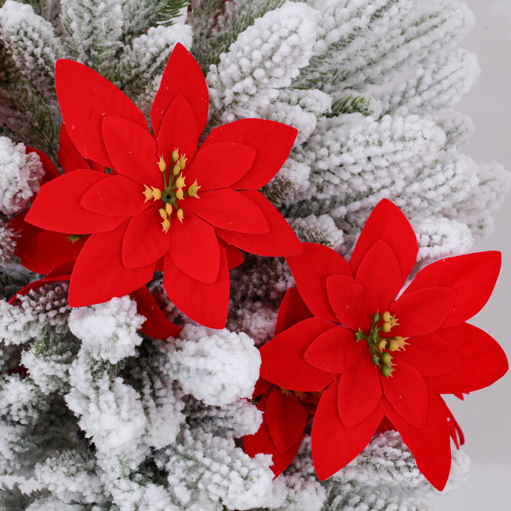 Closeup lifelike white artificial christmas tree with dense snow coating and vibrant red poinsettia blooms