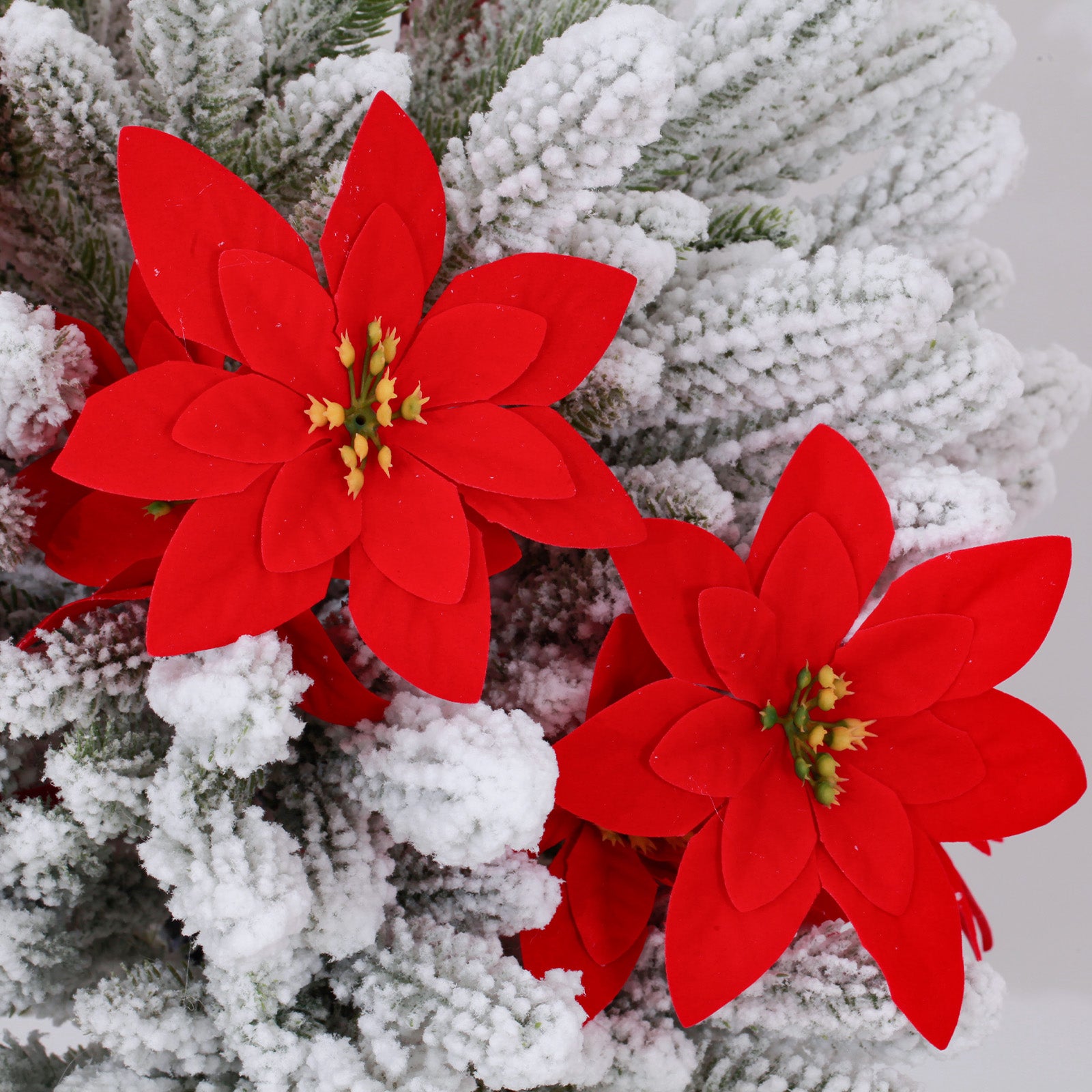 Closeup lifelike white artificial christmas tree with dense snow coating and vibrant red poinsettia blooms