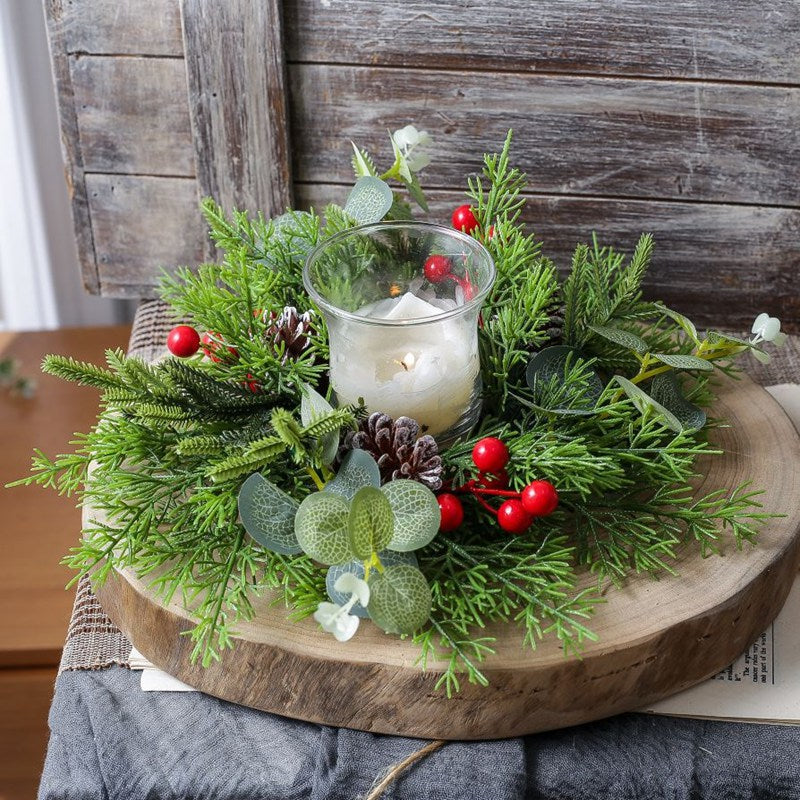 Holiday candle ring with cypress greenery, eucalyptus, pine cones and red berries displayed on large wooden slice with glass candle