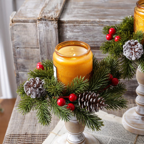 Christmas candle ring with pine branches, frosted pinecones and red berries, paired with amber jar candle on distressed wooden candlestick