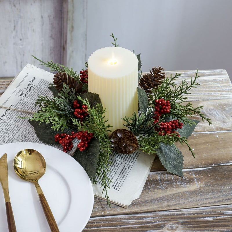 Artificial Christmas candle ring with pine cones, red berries and green foliage styled on wooden table with newspaper and gold cutlery