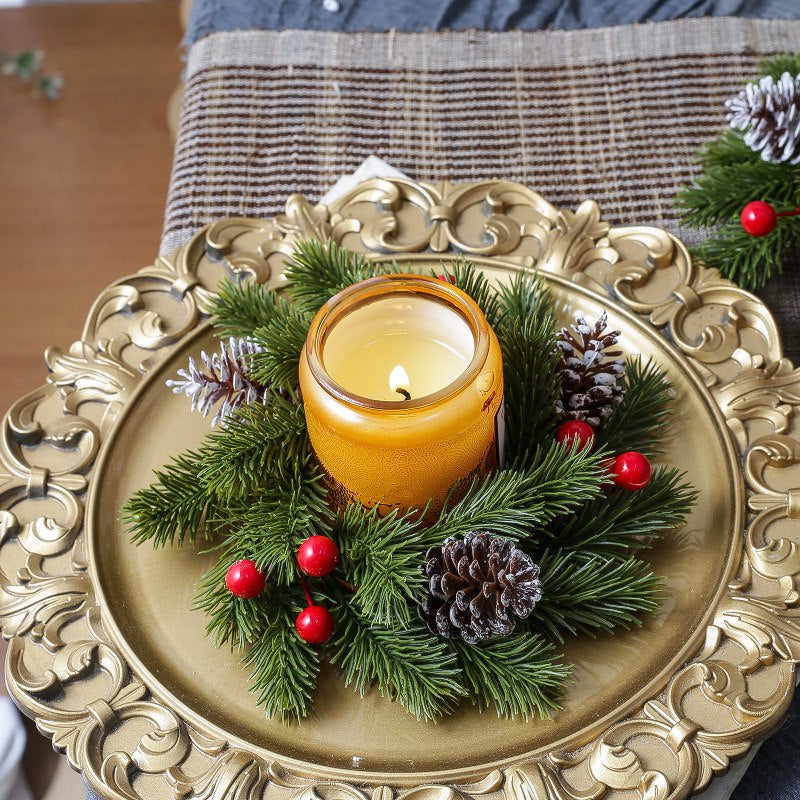 Christmas pine candle ring with red berries and frosted pinecones, amber candle set on ornate golden decorative plate