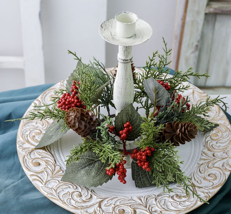 Greenery red berry pinecone candle ring placed around white distressed wooden candlestick on carved white and gold plate