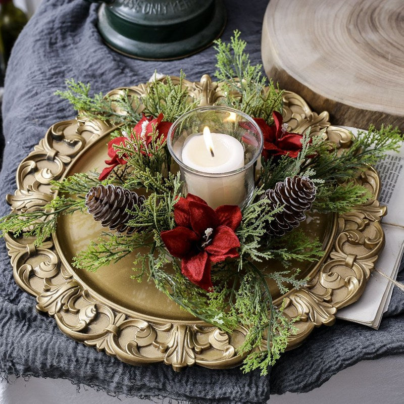 Christmas candle ring with red poinsettia flowers, frosted pinecones and cypress greenery around glass candle holder on ornate gold tray