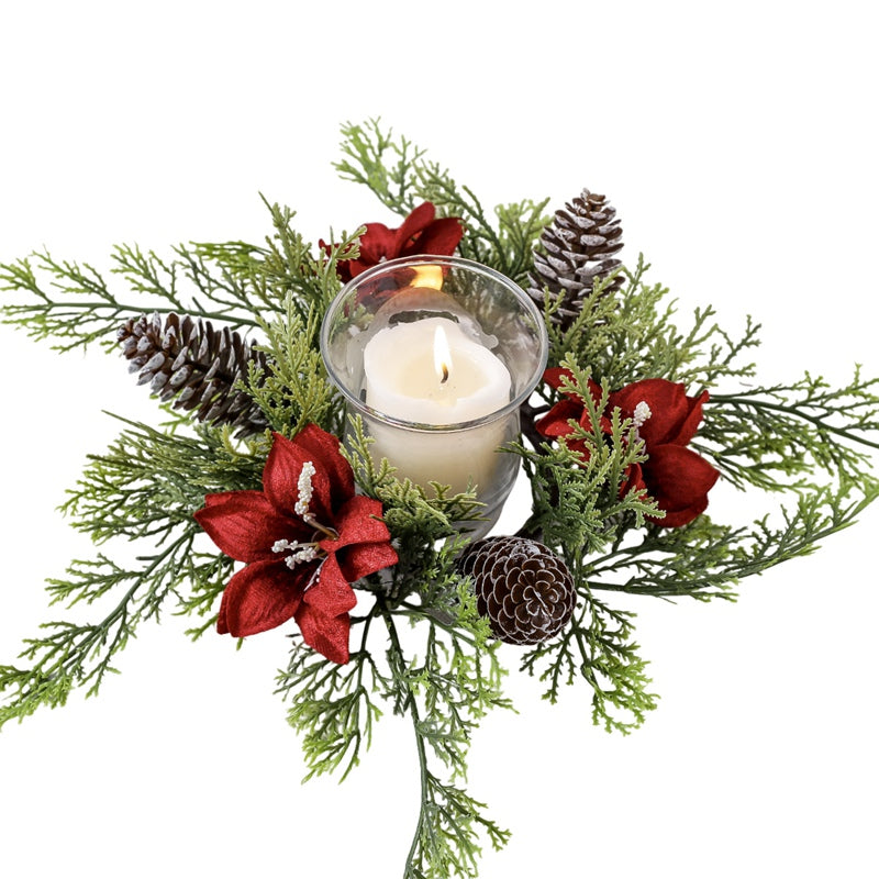 Top-down view of Christmas candle ring with red poinsettia, frosted pine cones and cypress greenery with glass candle on plain white background