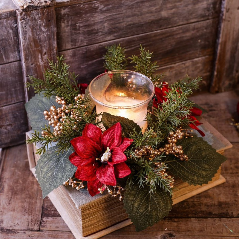 Festive poinsettia candle wreath with gold berries and cedar, paired with glass candle, placed on stacked vintage books for holiday table decor
