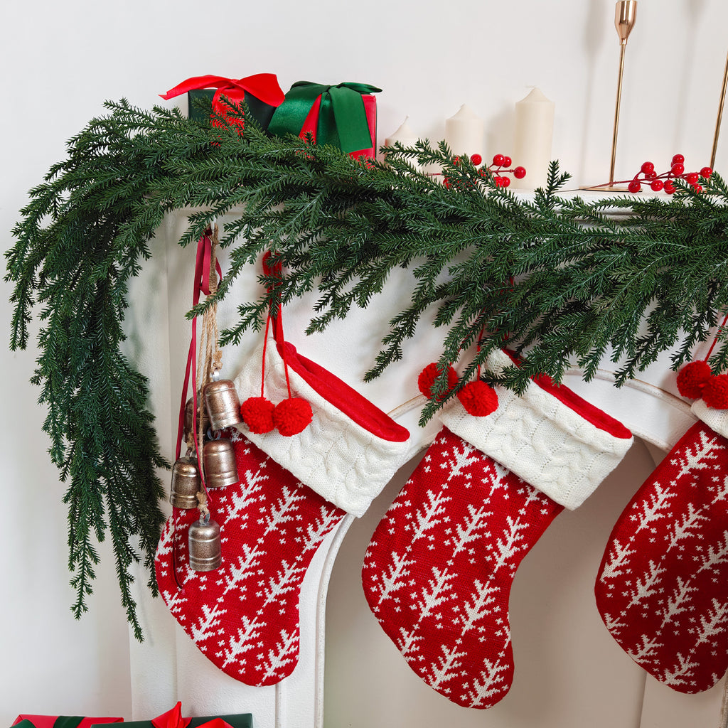 Textured norfolk pine faux xmas garland paired with red knit christmas stockings on carved white mantel