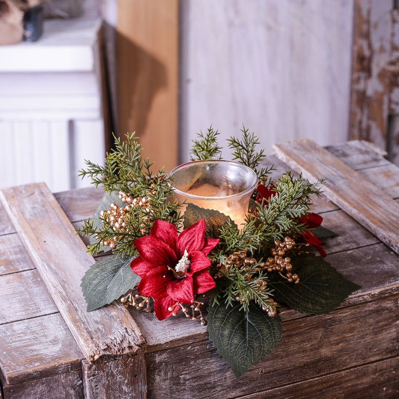 Christmas candle ring featuring red poinsettias, gold berries and cedar greenery around lit glass candle on weathered wooden crate