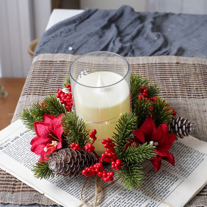 Artificial christmas candle ring wreath with red poinsettia, pine cones and berries encircling led pillar candle on vintage newspaper backdrop