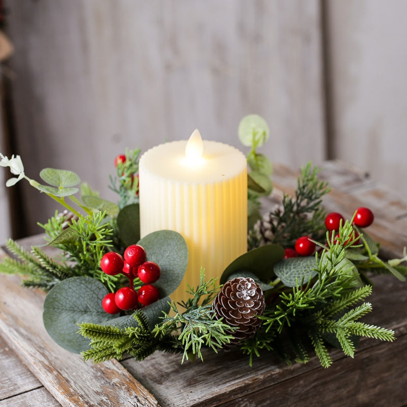 Close-up view of Christmas candle ring with eucalyptus leaves, red berries and frosted pine cone with lit pillar candle