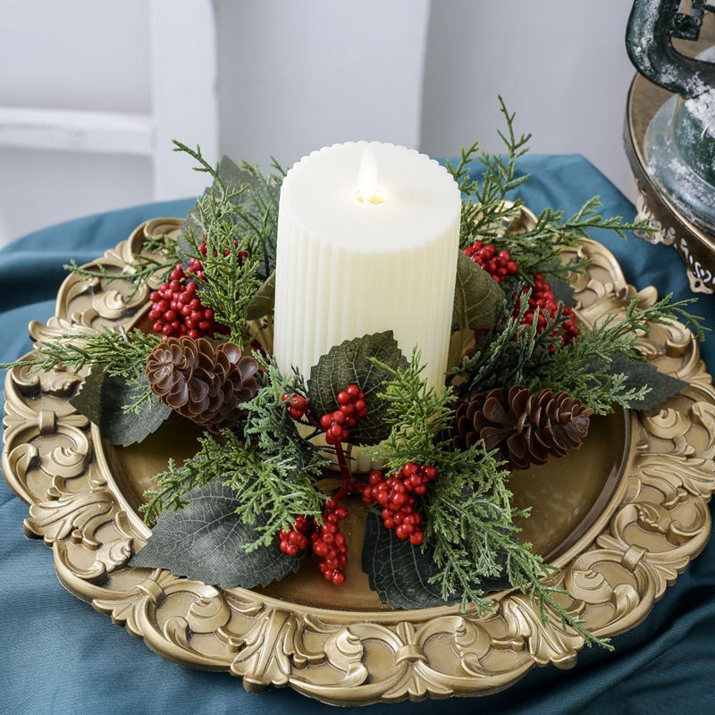 Holiday candle ring with cypress sprigs, red berries and pine cones paired with pillar candle on antique gold ornate plate over blue fabric