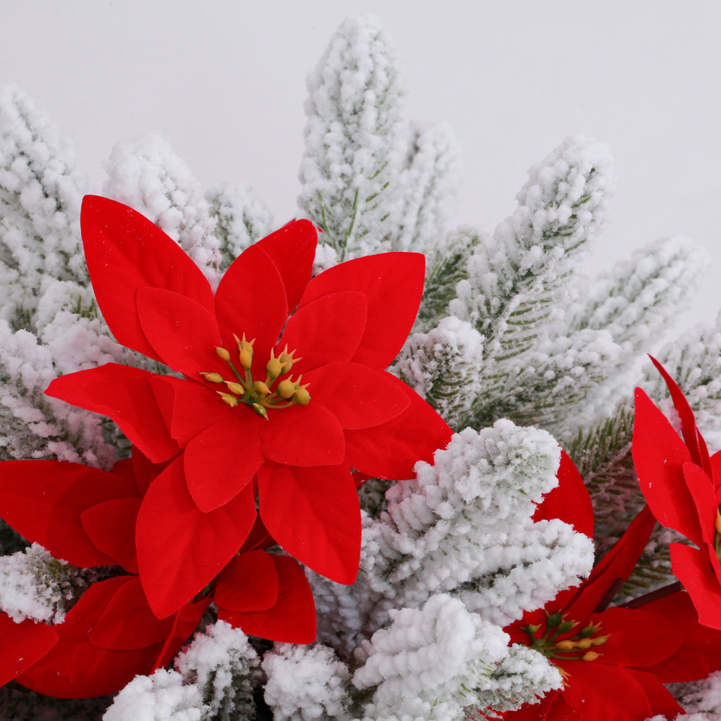 Closeup lifelike white artificial christmas tree with dense snow coating and vibrant red poinsettia blooms
