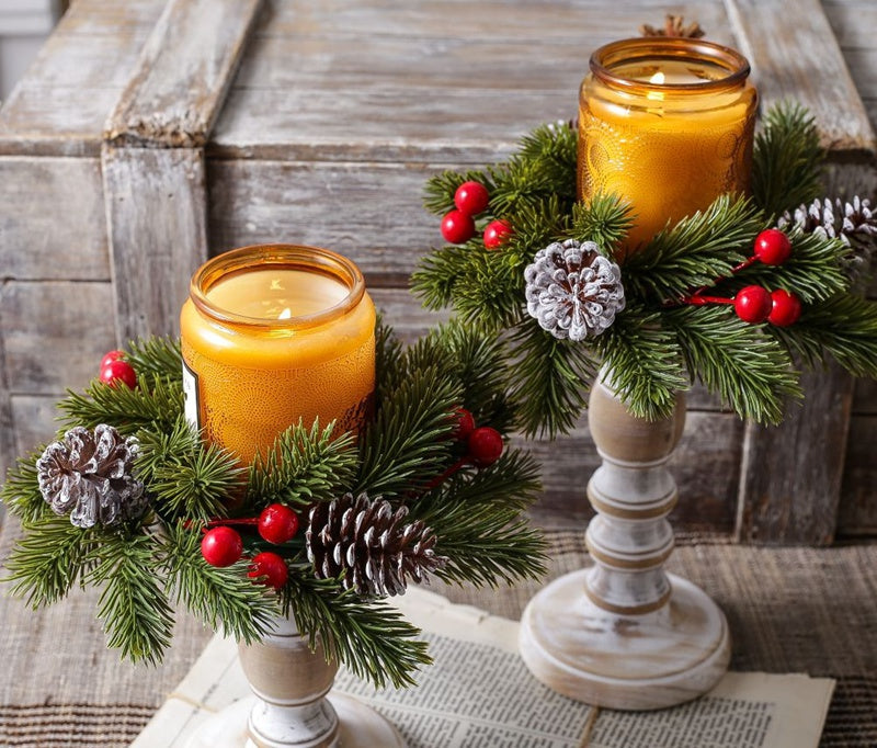 Set of two Christmas pine candle rings with red berries and frosted pinecones, amber candles on white wooden candlesticks