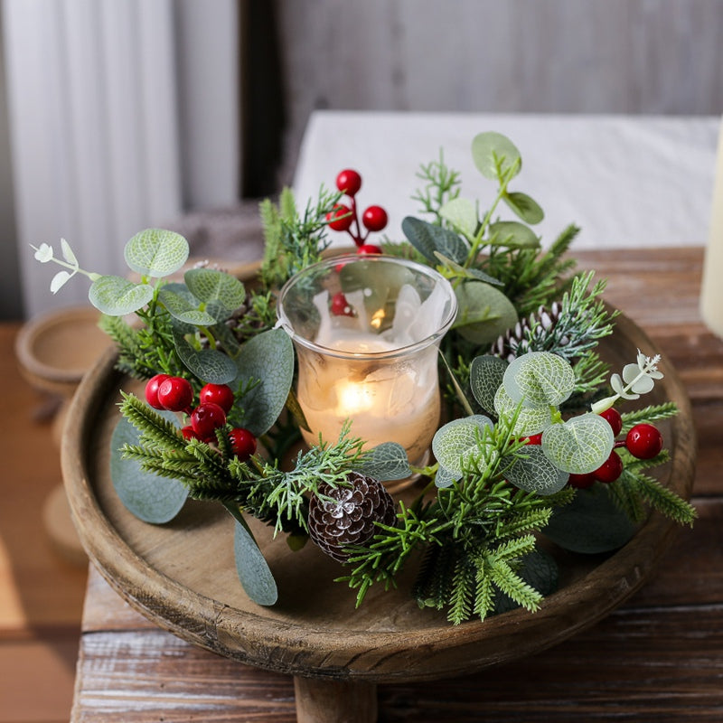 Holiday eucalyptus candle ring with pine cones and red berries surrounding glass candle holder on round wooden tray